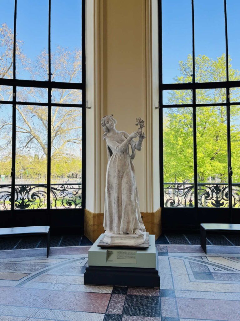Statue holding a flower in front of a large window at Petit Palais
